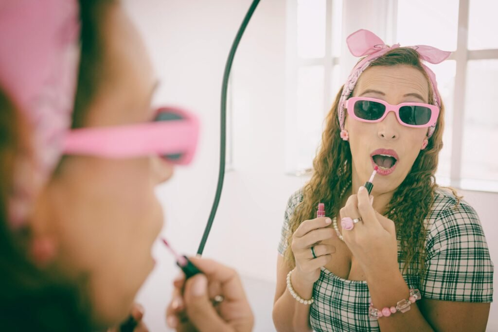 Fashionable woman in pink accessories applying lipstick, captured in a mirrored reflection.