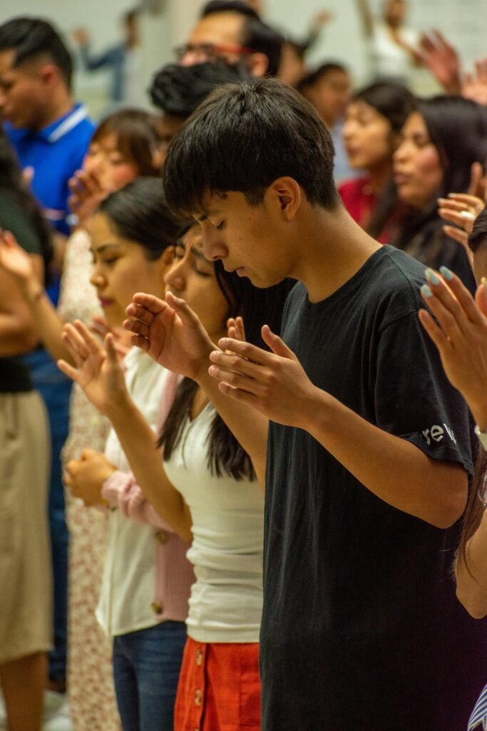 A diverse group of people standing in prayer with hands raised, focusing on worship.